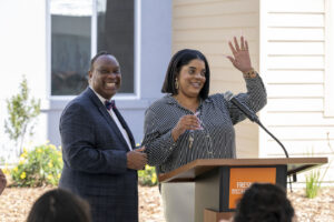 photo of a resident receiving the keys to her new home and waving to the crowd with the CEO of Fresno Housing